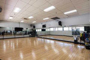 A spacious class room featuring wooden floors and numerous mirrors reflecting the bright, open atmosphere.